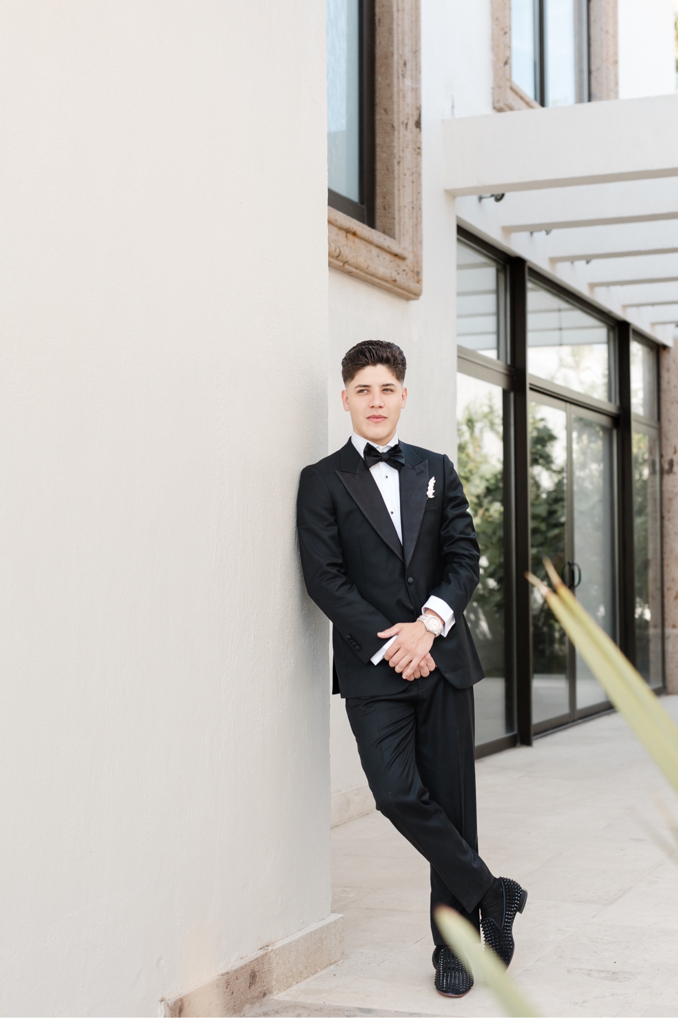 Larry Reyes Jr. in a black tuxedo and bow tie, leaning against a white wall